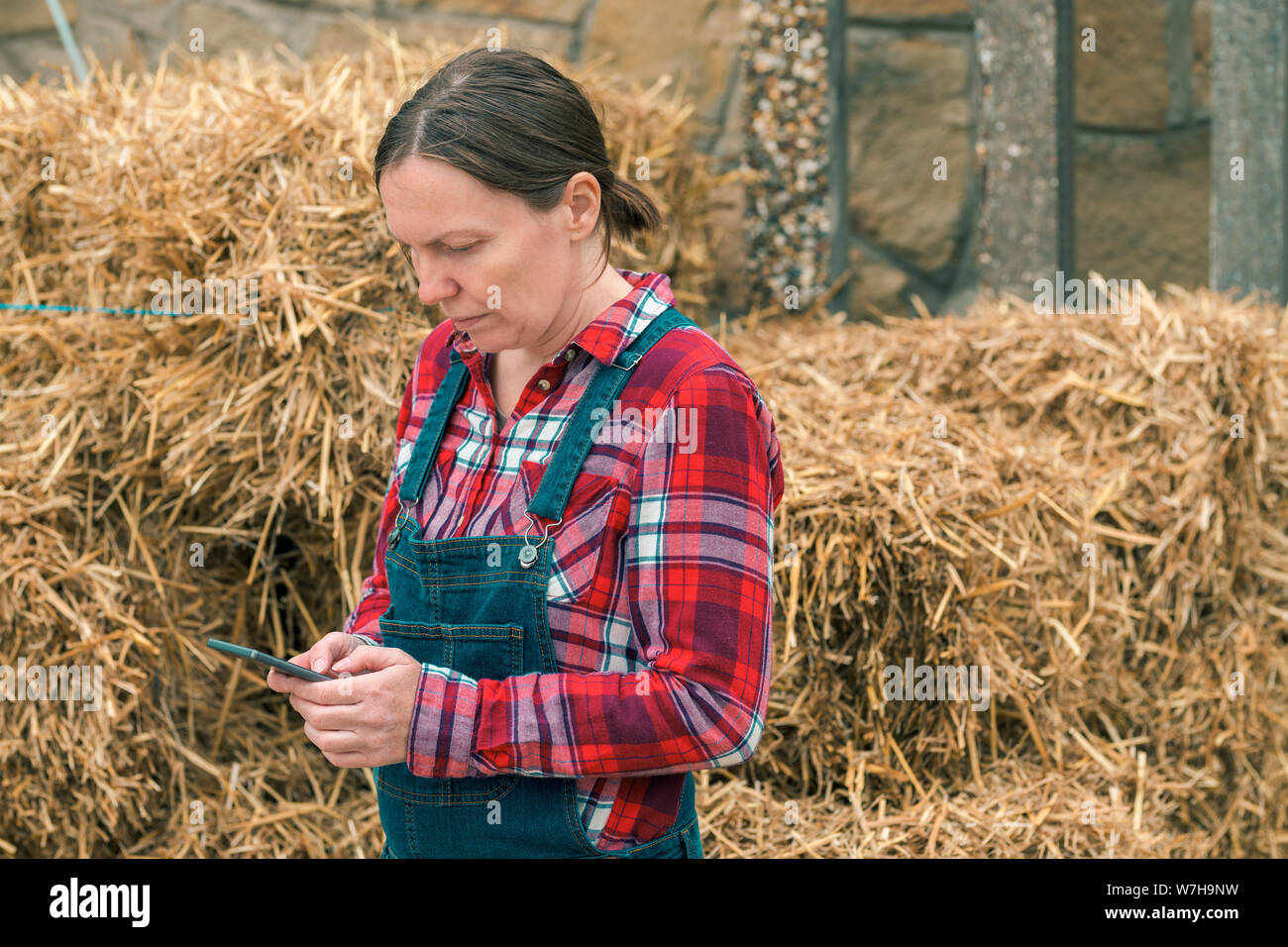 Frau Bauer Sie SMS auf Handy vor dem Bauernhaus Heuhaufen Stockfoto