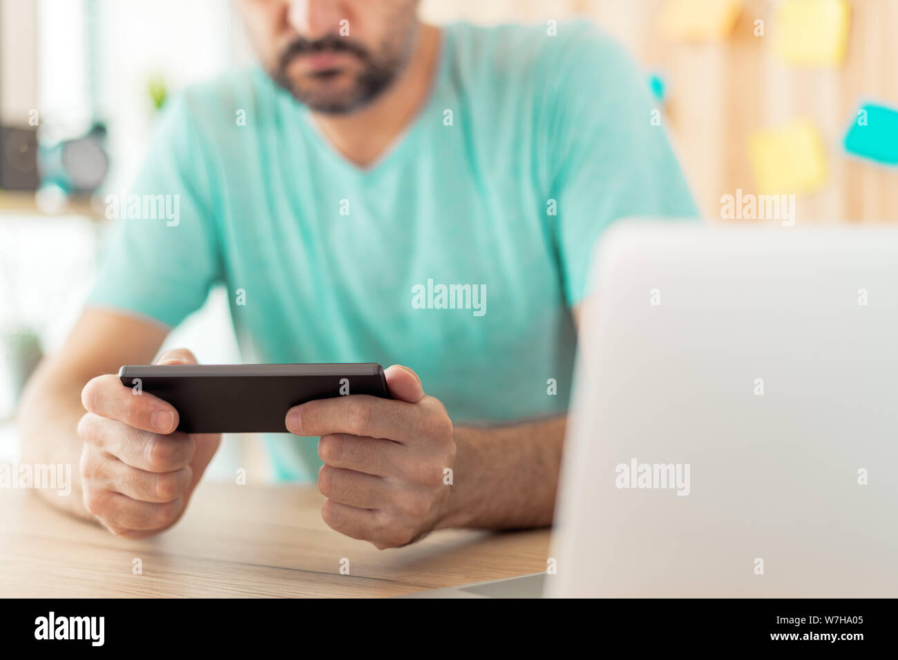 Freelancer spielen mobile video Spiel auf im Home Office smartphone. Casual männlichen erwachsenen Entspannung von der Arbeit mit unterhaltsamen Spiele App Stockfoto