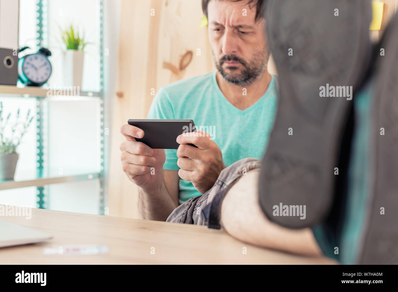 Freelancer spielen mobile video Spiel auf im Home Office smartphone. Casual männlichen erwachsenen Entspannung von der Arbeit mit unterhaltsamen Spiele App Stockfoto