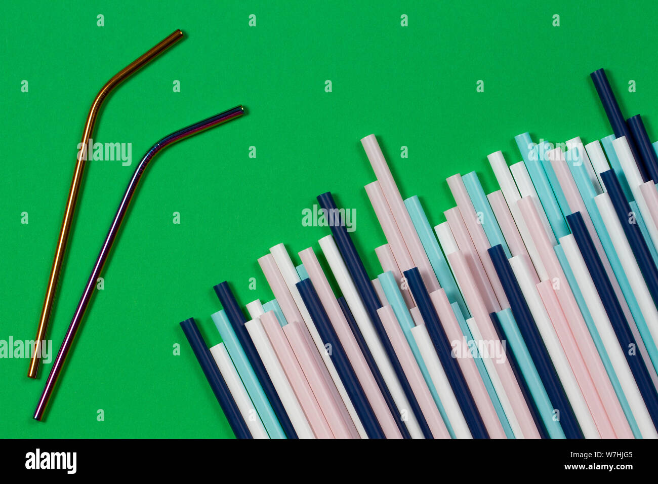 Zwei Edelstahl wiederverwendbare Trinkhalme mit viele bunte Plastik Strohhalme auf grünem Hintergrund Stockfoto