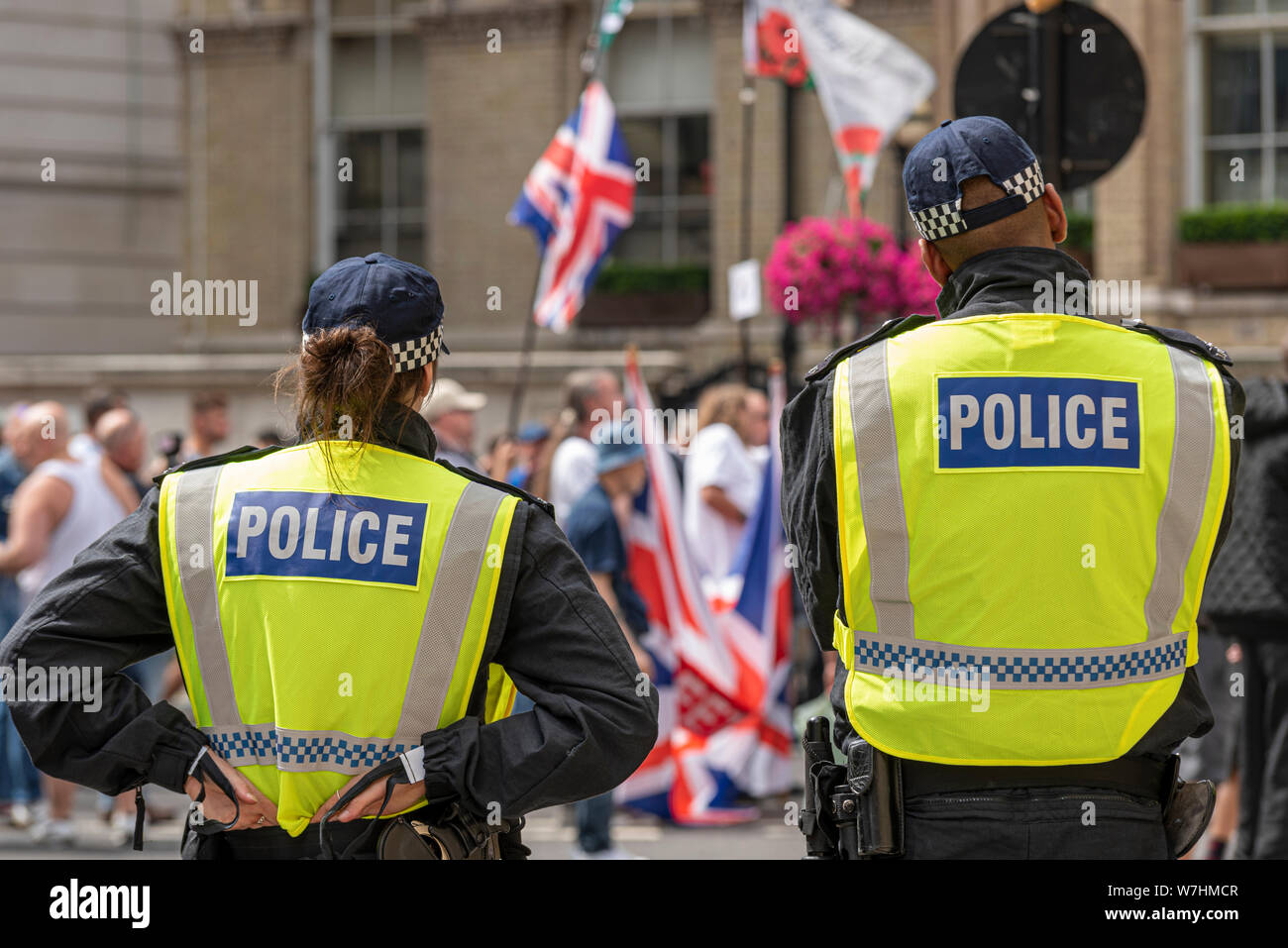 Die polizeiliche Überwachung der demonstranten am Freien Tommy Robinson Protestkundgebung in London, UK. Beobachten. Weibliche und männliche Führungskräfte. Union Jack Flags Stockfoto