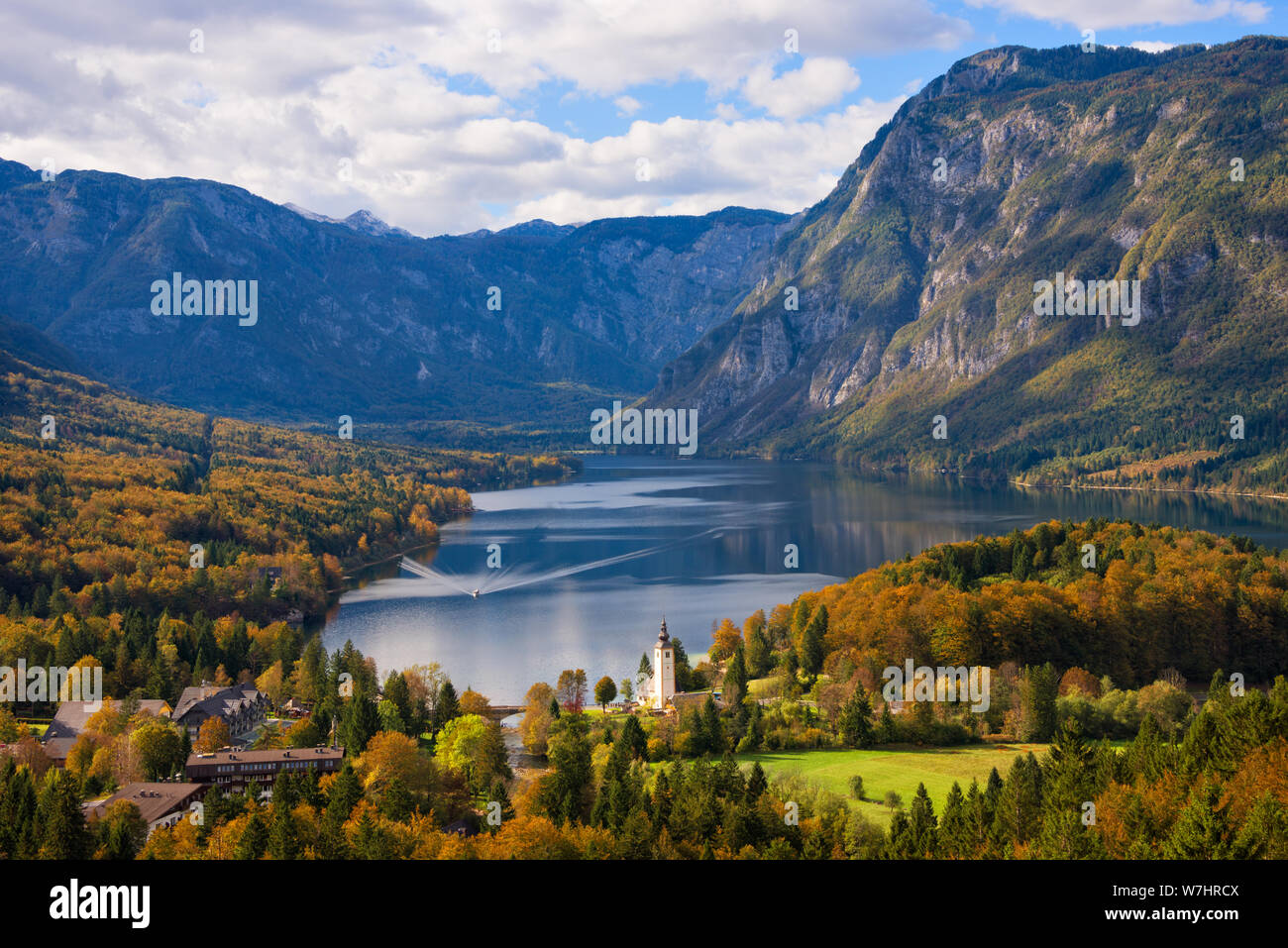 Eine Fähre in Richtung der Stadt Ribčev Laz am See Bohinj und Bäume im Herbst Farben und Julischen Alpen Berge im Herbst Landschaften in Slowenien. Stockfoto