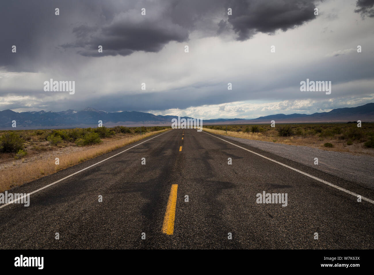 Die gelben Linien einer zweispurigen Autobahn, US Highway 50, unter bewölktem Himmel in der Mitte der Wüste an der Grenze zu Utah Nevada im Sommer aft Stockfoto