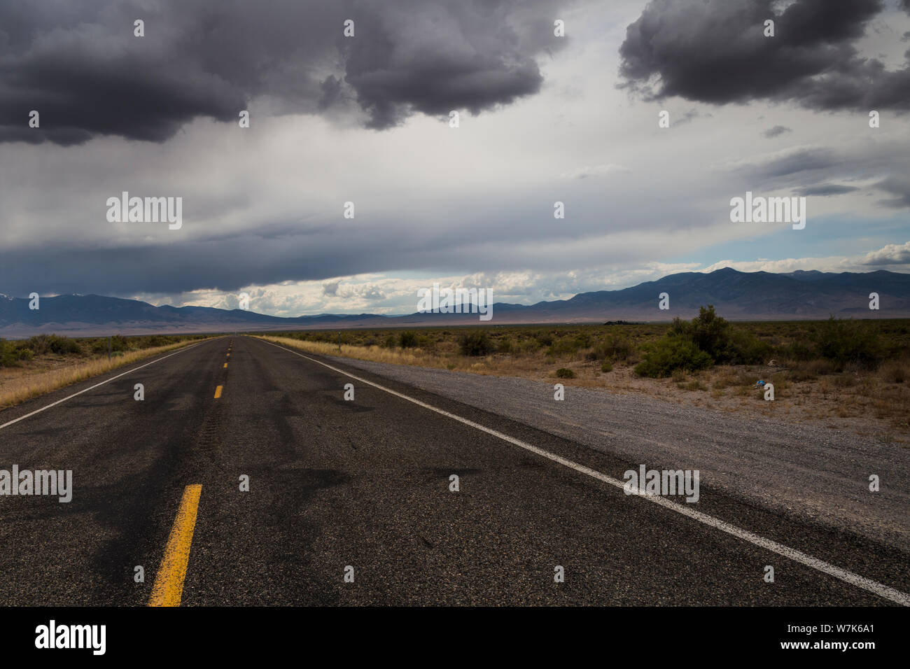 Die gelben Linien einer zweispurigen Autobahn, US Highway 50, unter bewölktem Himmel in der Mitte der Wüste an der Grenze zu Utah Nevada im Sommer aft Stockfoto