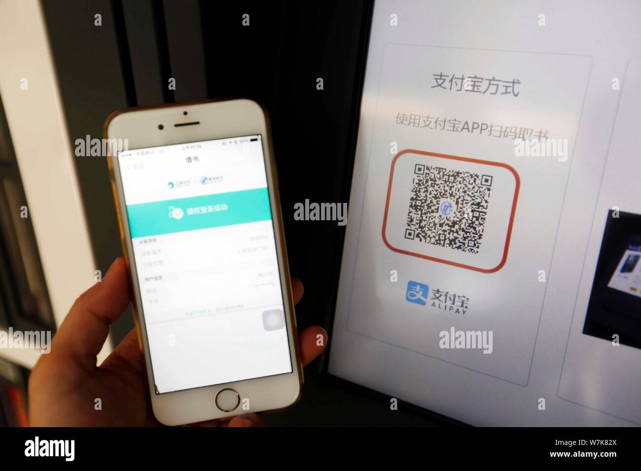 Ein Bürger Scans einen QR-Code über Mobile Payment Service Alipay von Alibaba Group auf Ihrem Smartphone zu Bücher kostenlos vor einem gemeinsamen Bücherregal ausleihen Stockfoto