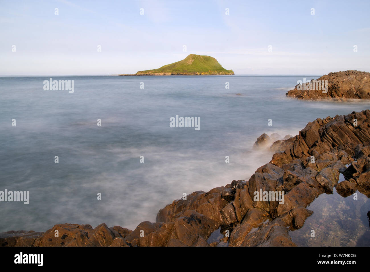 Lange Belichtung von Kalksteinfelsen, die von Wellen mit dem Kopf der Wurm im Hintergrund gewaschen, abgeschnitten vom Festland auf eine Insel bei Flut, Rhossili, die Halbinsel Gower, Wales, Großbritannien, Juli. Sequenz 3 von 3 Passende Ansichten zu verschiedenen Gezeiten Stockfoto