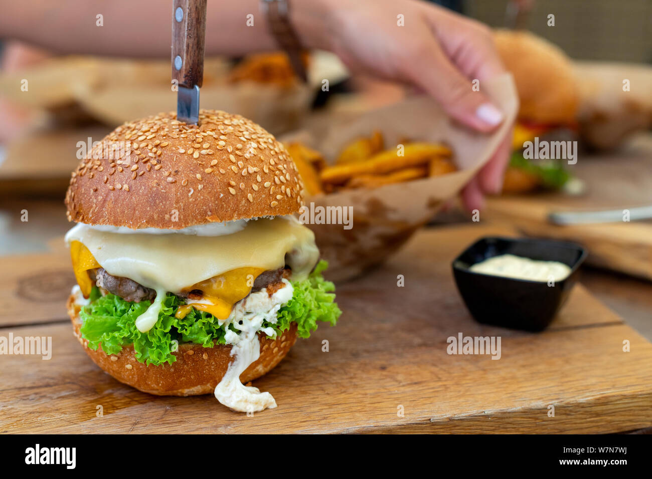 Bild von einem köstlichen saftigen Cheeseburger mit Keilen und Sauce Tartar auf hölzernen Platte serviert. Stockfoto