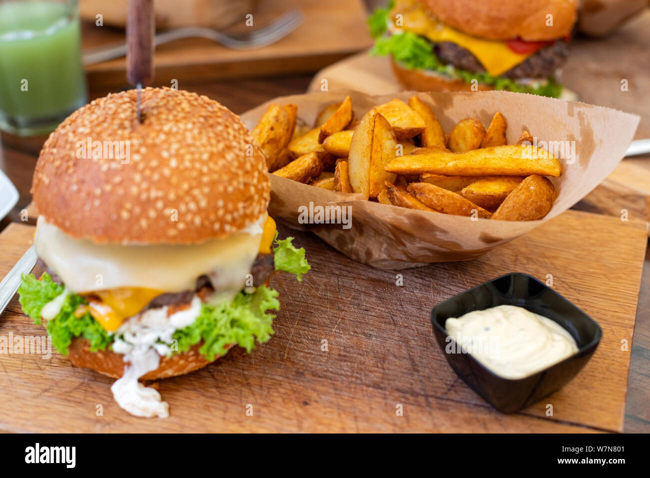 Bild von einem köstlichen saftigen Cheeseburger mit Keilen und Sauce Tartar auf hölzernen Platte serviert. Stockfoto