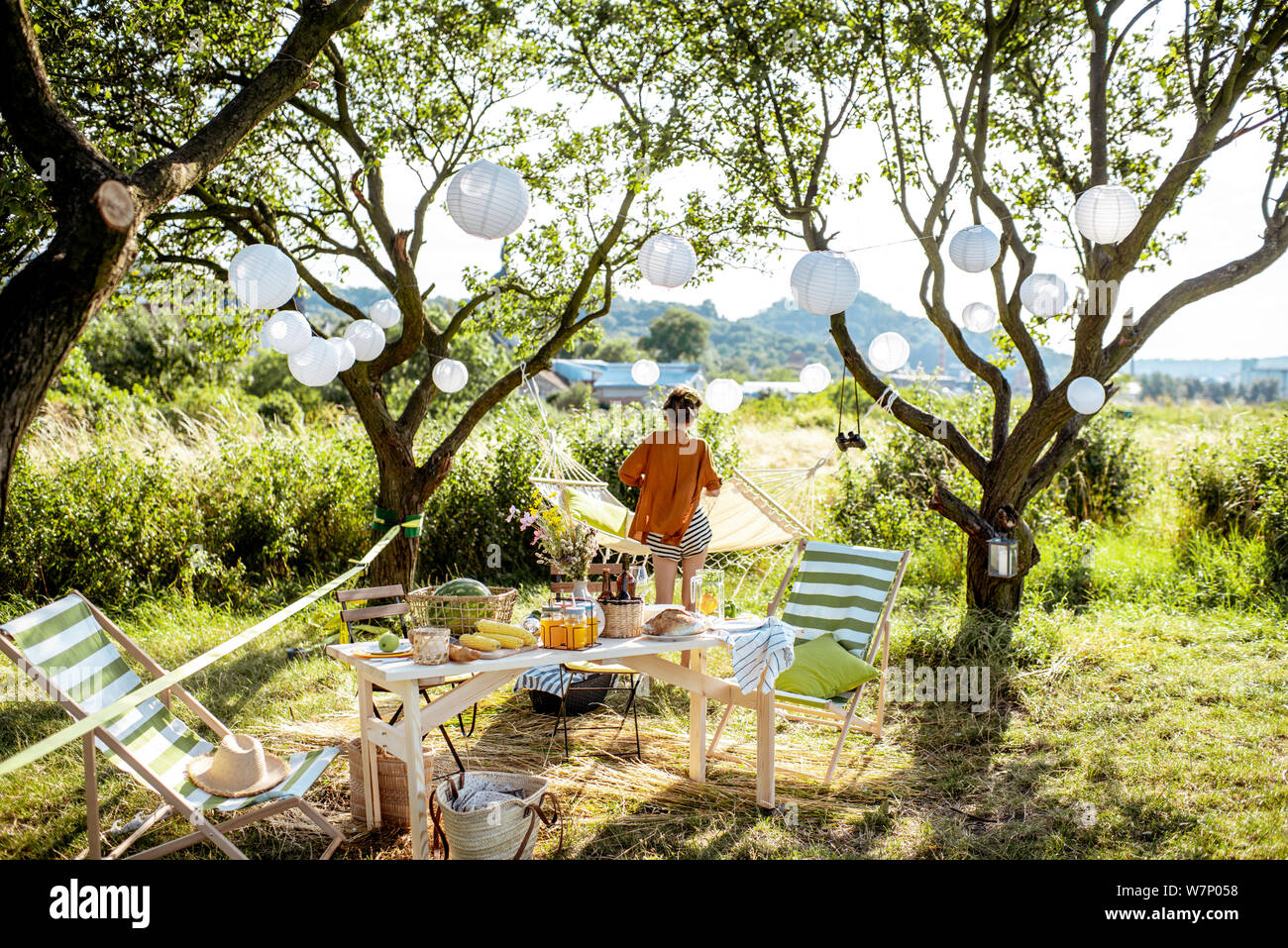 Schön Garten mit Sonnenliegen, Tisch, Hängematte und dekorative Laternen,  bereit für den festlichen Abendessen eingerichtet. Frau auf dem Hintergrund  Stockfotografie - Alamy