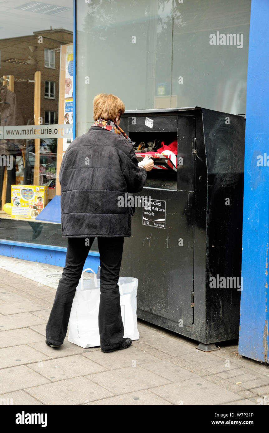 Frau recycling Kleidung Kleidung in eine Bank außerhalb der Liebe shop, Highbury Corner, Londoner Stadtteil Islington, Großbritannien Stockfoto