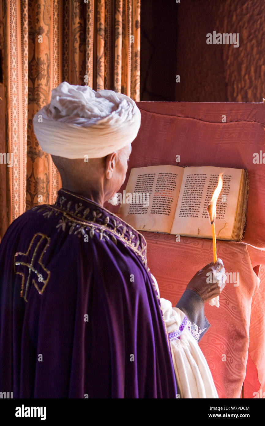 Priester, die eine Kerze und das Lesen der 900 Jahre alten Heiligen Buch von Gabriel in Wette Gabriel-Rufael, einer der berühmten lalibela's Rock-gehauenen Kirchen, Lalibela zählt zu einer der größten christlichen der Welt religiös-historischen Stätten, Lalibela, Äthiopien 2005 Stockfoto