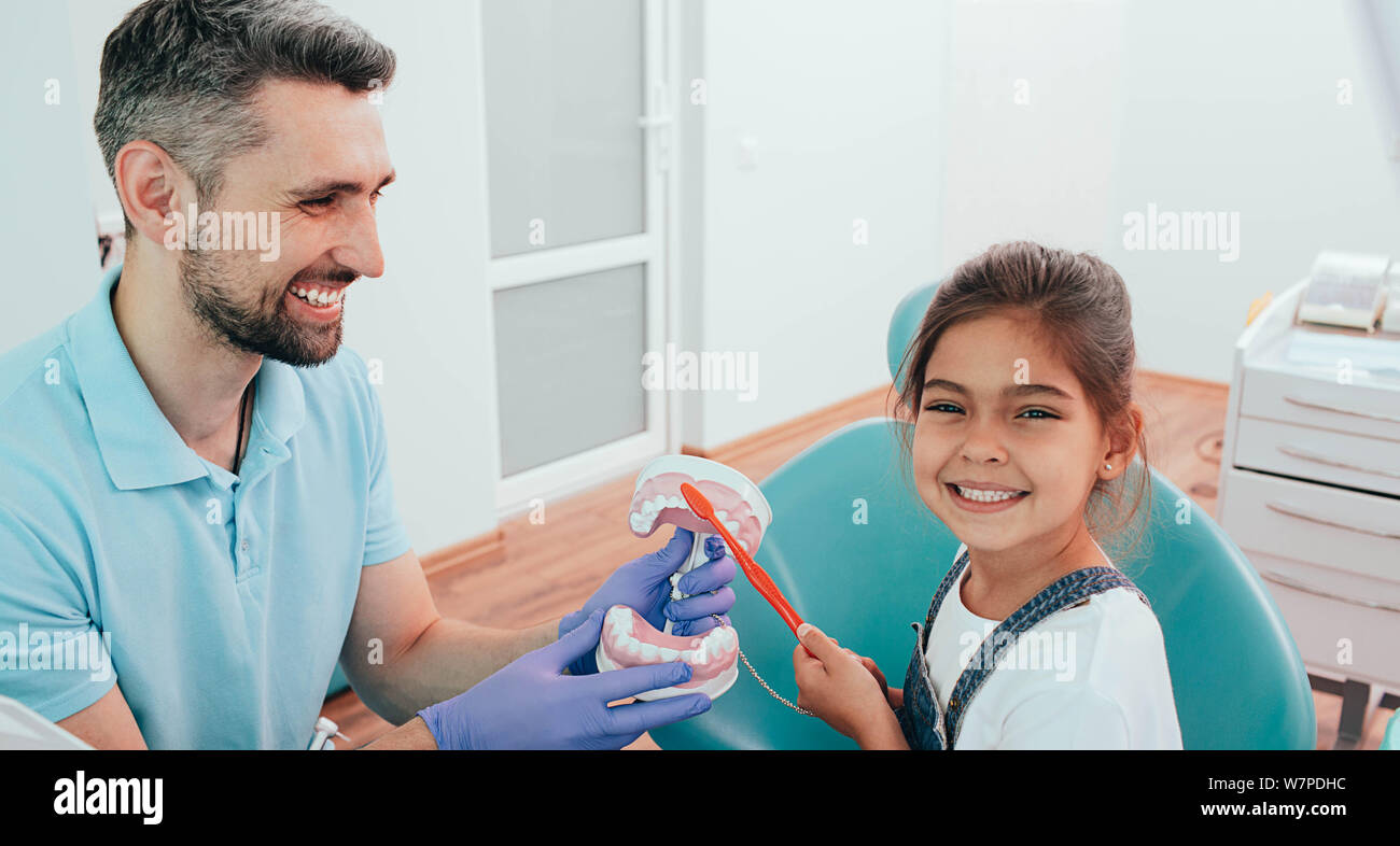 Zahnarzt Lehre wenig gemischten Rennen Mädchen Zähneputzen mit menschlichen Zähne Modell auf zahnmedizinische Klinik Stockfoto