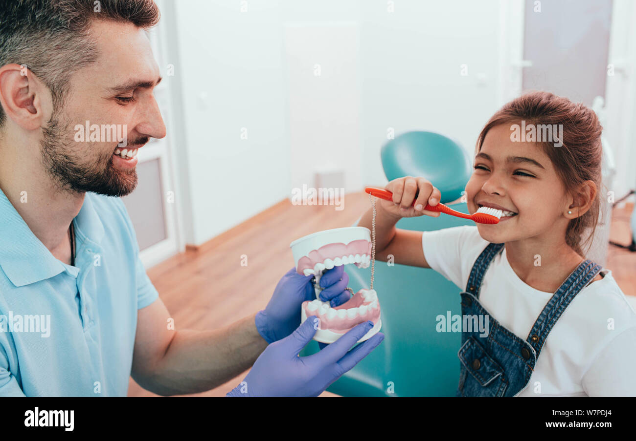 Zahnarzt Lehre wenig gemischten Rennen Mädchen Zähneputzen mit menschlichen Zähne Modell auf zahnmedizinische Klinik Stockfoto
