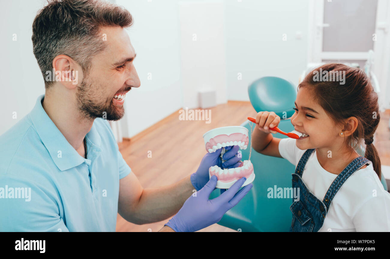 Zahnarzt Lehre wenig gemischten Rennen Mädchen Zähneputzen mit menschlichen Zähne Modell auf zahnmedizinische Klinik Stockfoto