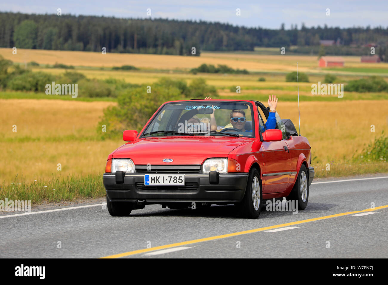 Vaulammi, Finnland. August 3, 2019. Familie lächelnd und winkend auf dem 1990s rot Ford Escort Cabrio auf Maisemaruise2019 Auto Kreuzfahrt. Credit: Taina Sohlman Stockfoto