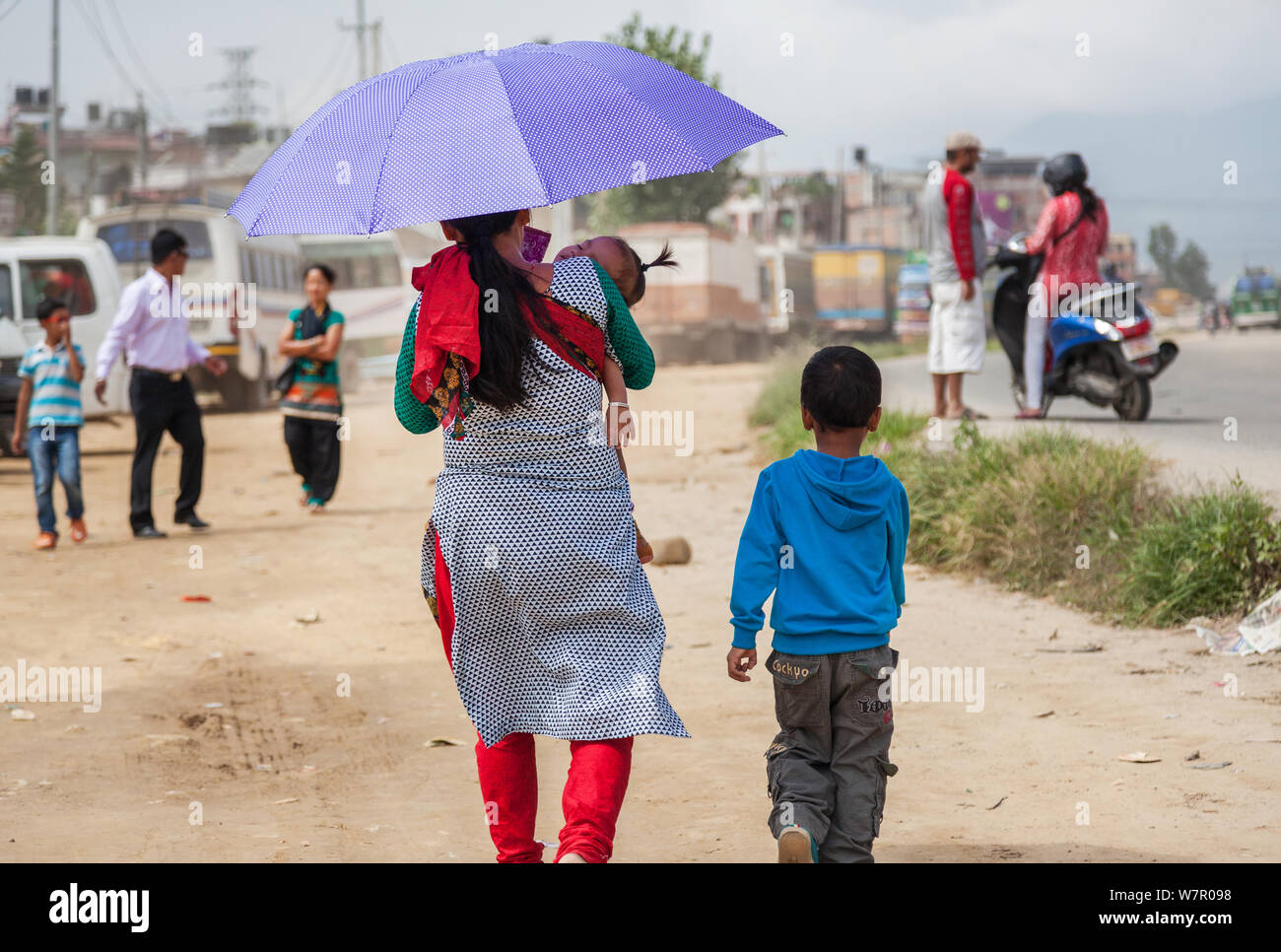 Mutter und Kind mit Regenschirm ihr Baby an der Seite einer städtischen Straße in Kathmandu. Stockfoto