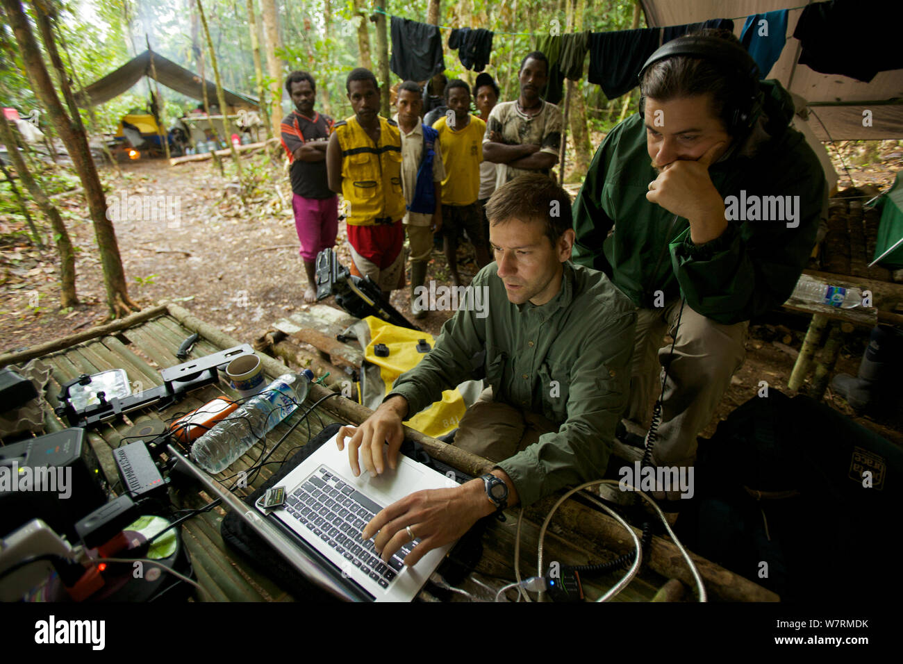 Eric Liner Bewertungen Filmmaterial auf seinem Laptop, während Edwin Scholes und Dorfbewohner auf. West Papua, Neuguinea, August 2009 Stockfoto
