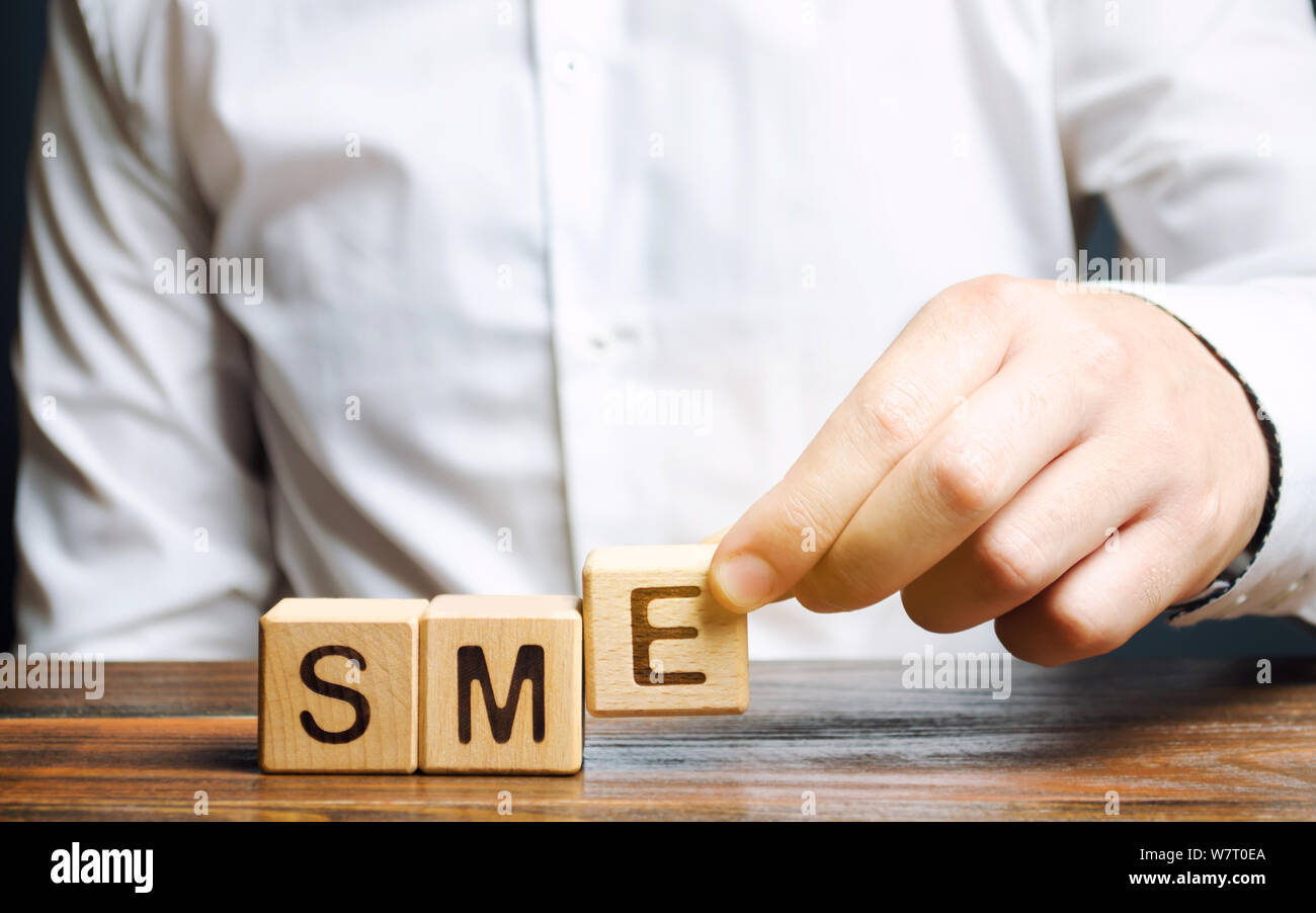 Unternehmer hält Holzblöcke mit dem Wort KMU. Kleine und mittlere Unternehmen, gewerbliche Unternehmen, die nicht bestimmte Indikatoren nicht überschreiten. Stockfoto