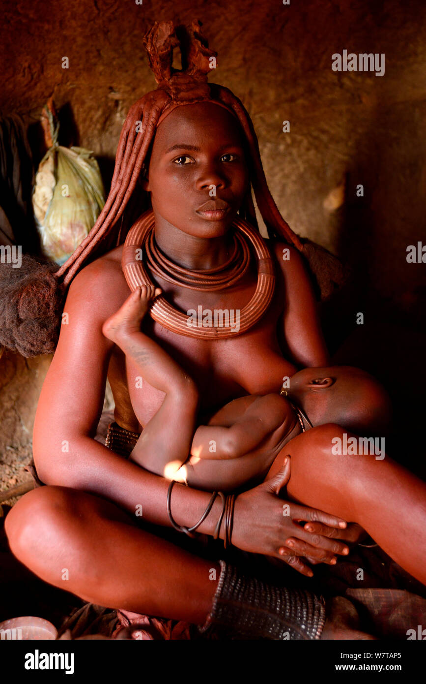 Frau Himba ihr Baby stillen in ihrer Hütte. Kaokoveld, Namibia, September 2013. Stockfoto