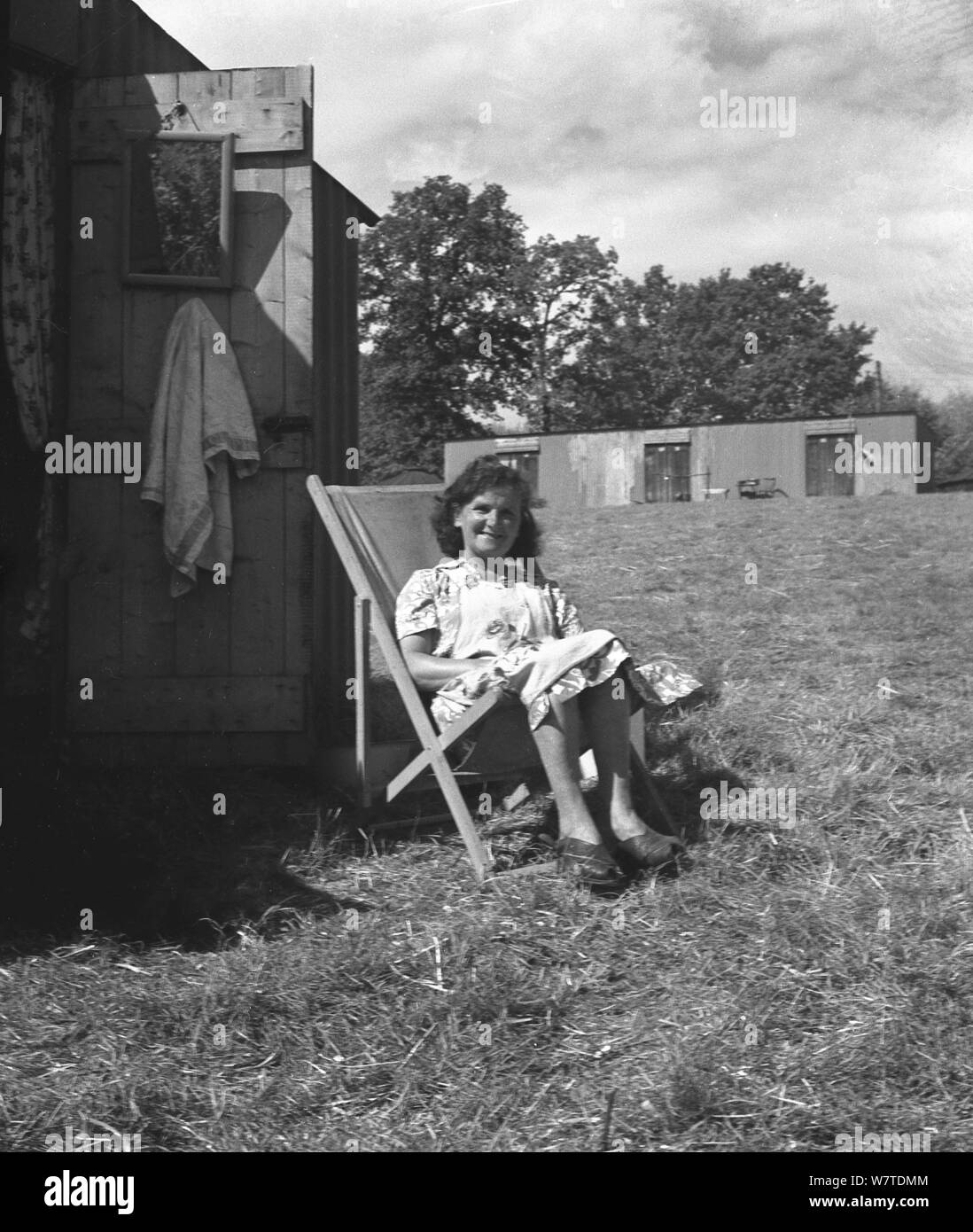 1951, historische, eine Dame landwirtschaftliche Arbeiter, ein Hop picker außerhalb ihrer Kabine oder Quartiere in einem Stuhl sitzend in ein Feld in eine Pause von der Arbeit, Kent, England, UK. Stockfoto