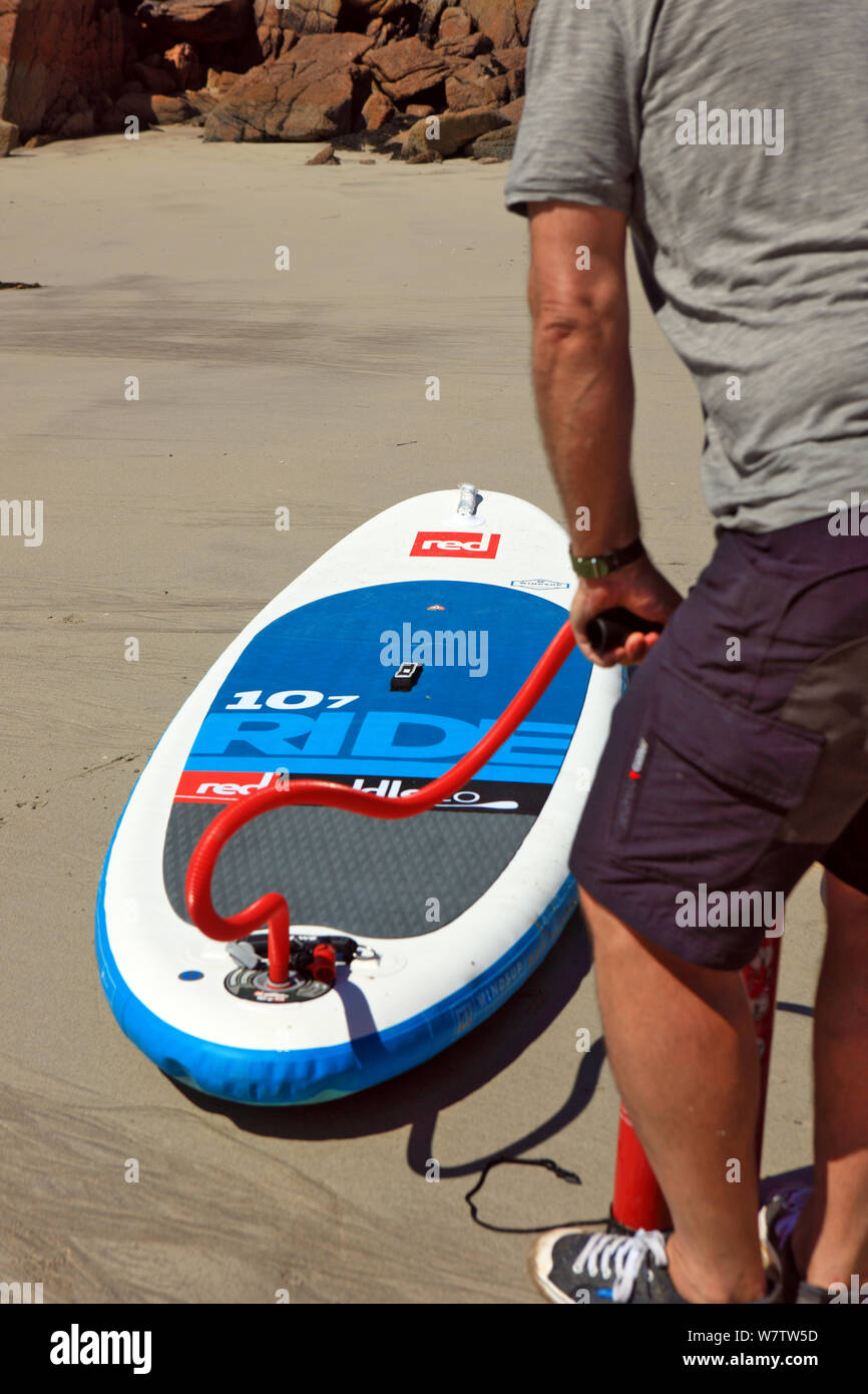 Mann, der am Strand ein Paddelbrett aufbläst, UKbeacg Stockfoto
