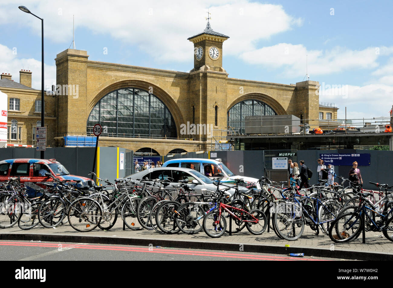 Fahrräder Fahrradständer befestigt vor Taxis und Verkehr mit King's Cross Station hinter, London, England, Großbritannien, Juli 2013. Stockfoto