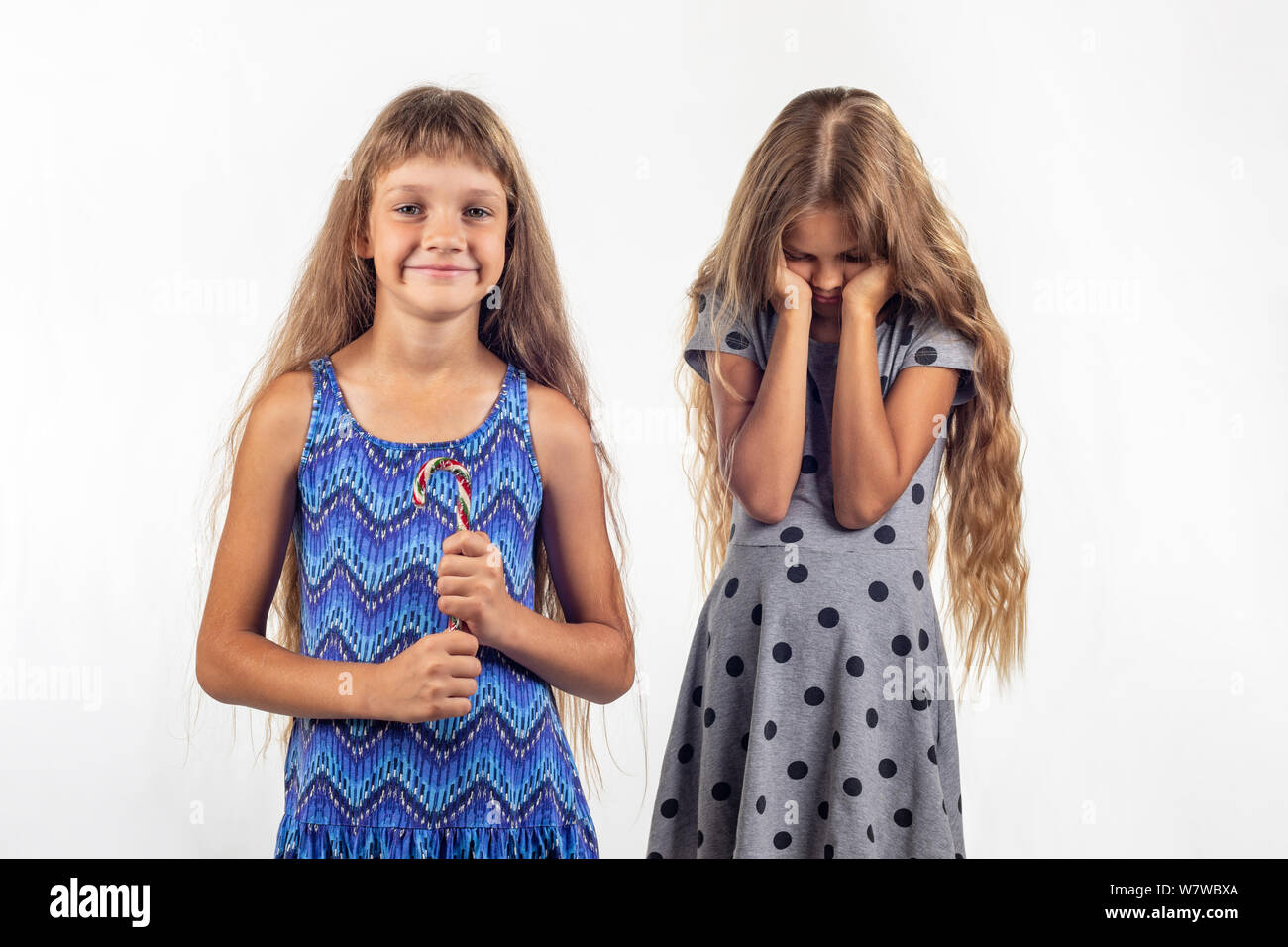 Mädchen hält freudig Süßigkeit, traurig, andere Mädchen im Hintergrund Stockfoto