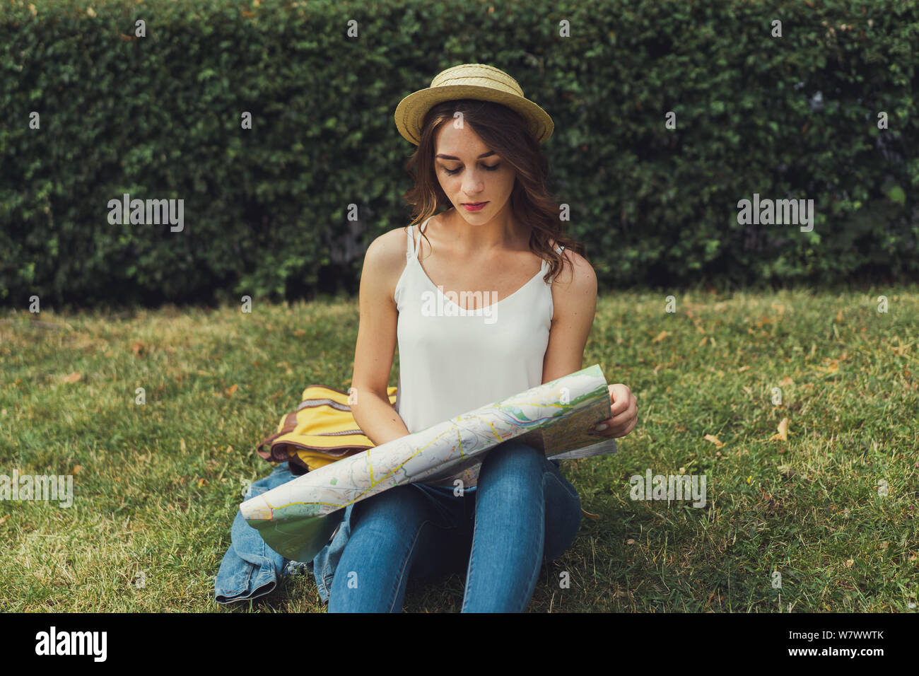 Schöne junge Frau sitzt auf Gras genießen Sie sonnige Tag im Park. Sommer glücklichen Moment. Auf der Suche nach etwas auf der Karte. Stockfoto