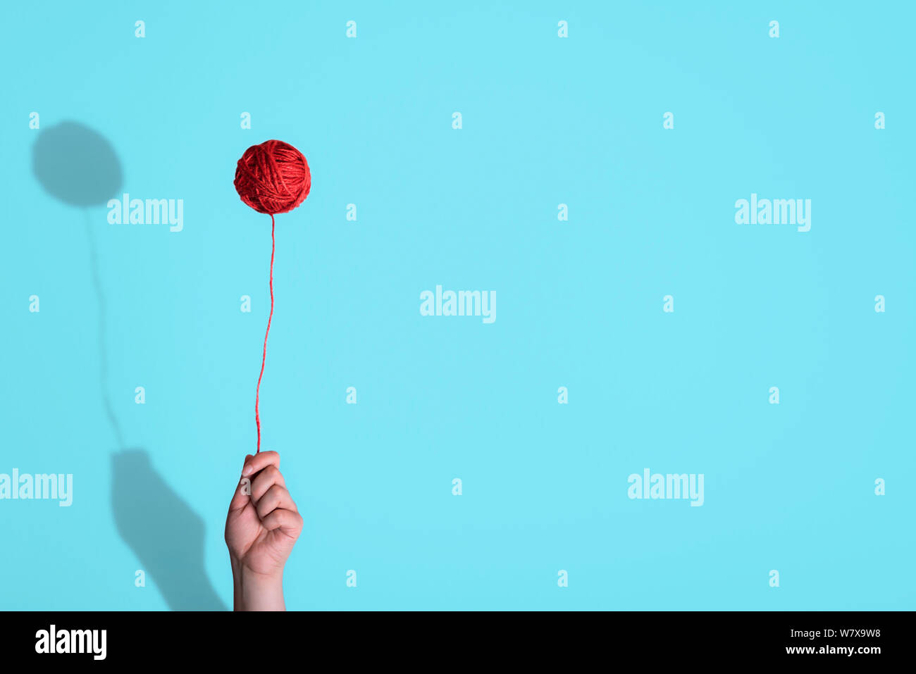 Frau hand mit einem schwebenden roten Faden Kugel, wie ein Ballon vor einem blauen Hintergrund. Minimalistische Kunsthandwerk Konzept. Sonderbar Ballon. Kindheit frame Stockfoto