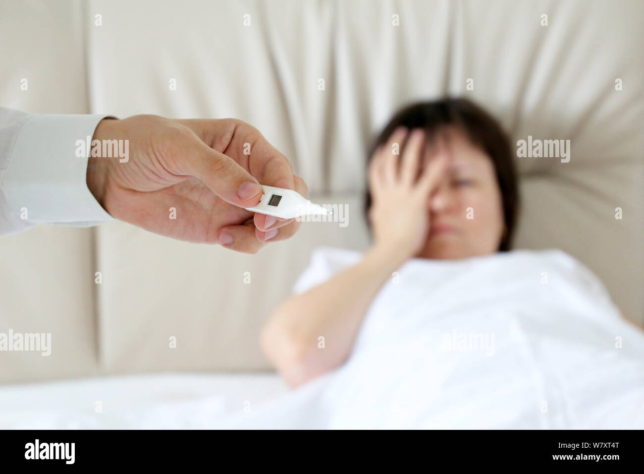 Kranke Frau in einem Bett liegen, digitale Thermometer in männlicher Hand. Arzt Messung der Körpertemperatur des Patienten, Konzept der Erkältung und Grippe, Fieber, Krankheit Stockfoto