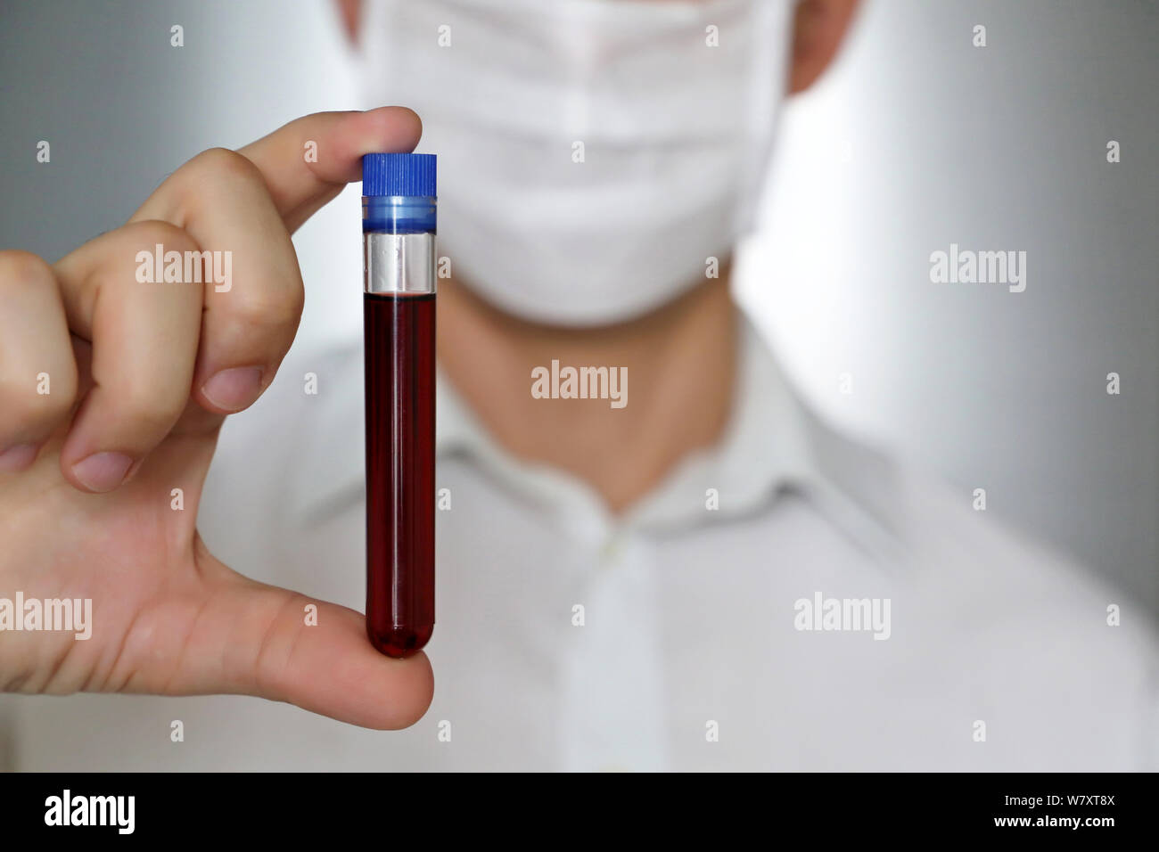 Der Mensch in der medizinischen Maske mit einem Reagenzglas in der Hand. Konzept der Blutprobe, medizinische und chemische Forschung, Impfung, Arzt oder Wissenschaftler Stockfoto