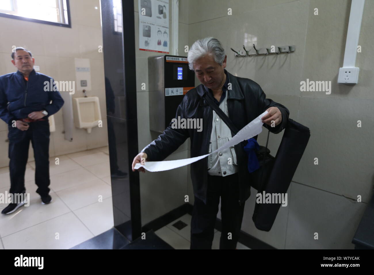 Ein chinesischer Mann sieht den freien Toilettenpapier von der Maschine auf der Wand durch sein Gesicht Scannen in Tiantan Park, Peking, 18. März 2017. Stockfoto