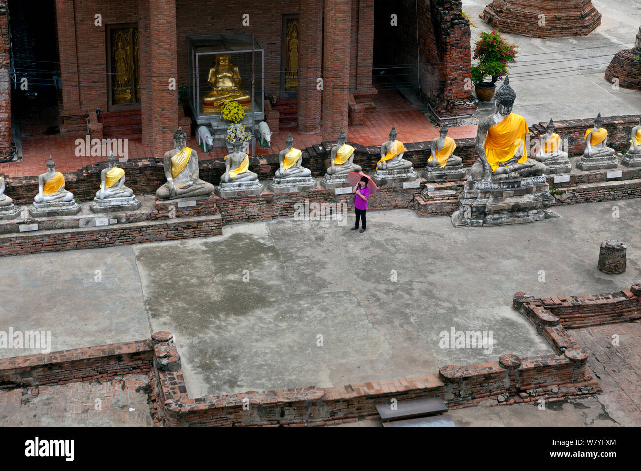 Reihe von Buddhas mit gelben Schärpen, und die Frau am Telefon, Wat Yai Chaya Mongkol, Ayutthaya. Thailand, September 2014. Stockfoto