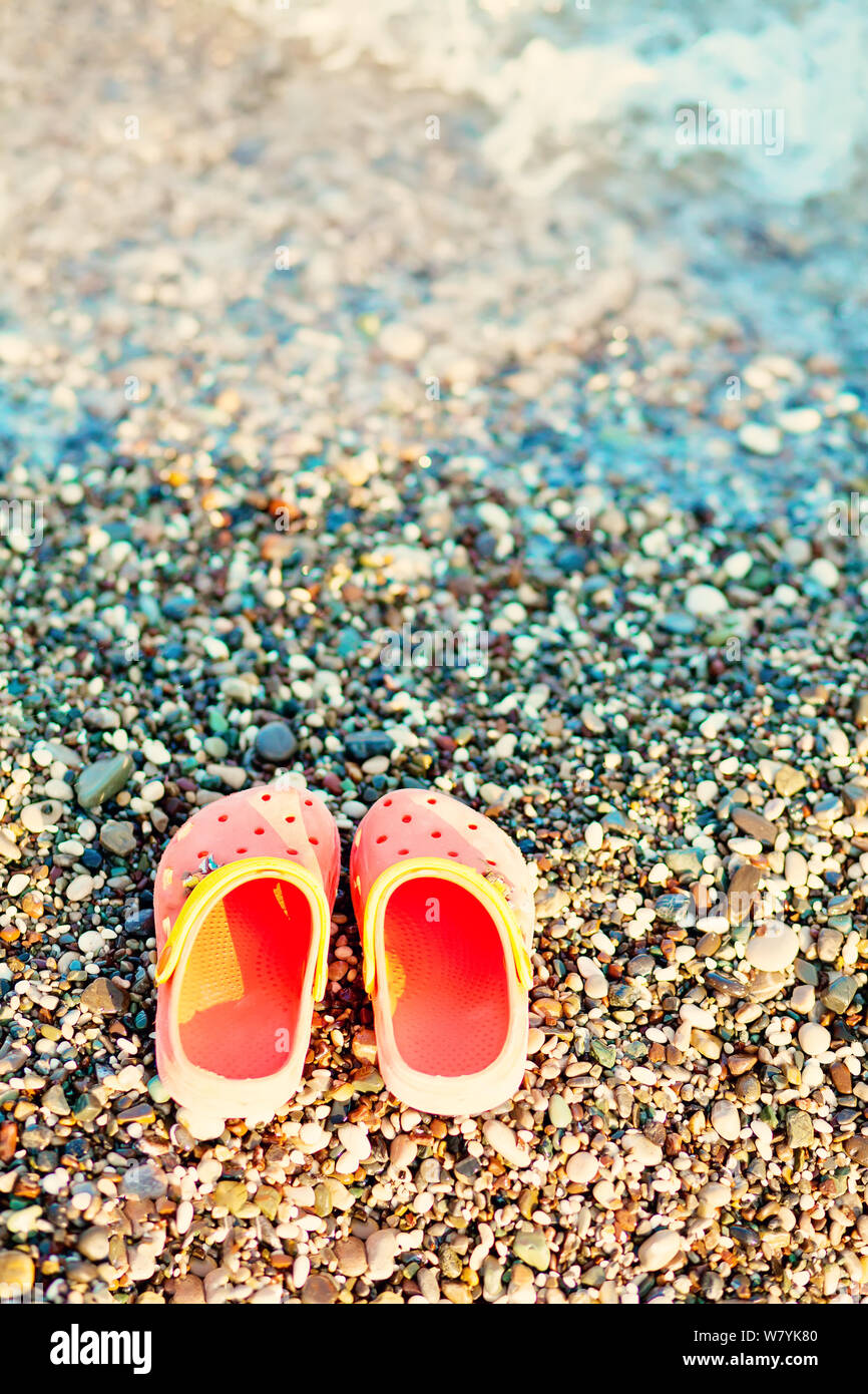 Paar orange Sandalen Kid's von einem Schwimmer in einem Strand in der Nähe des Meeres im Sommer Stockfoto