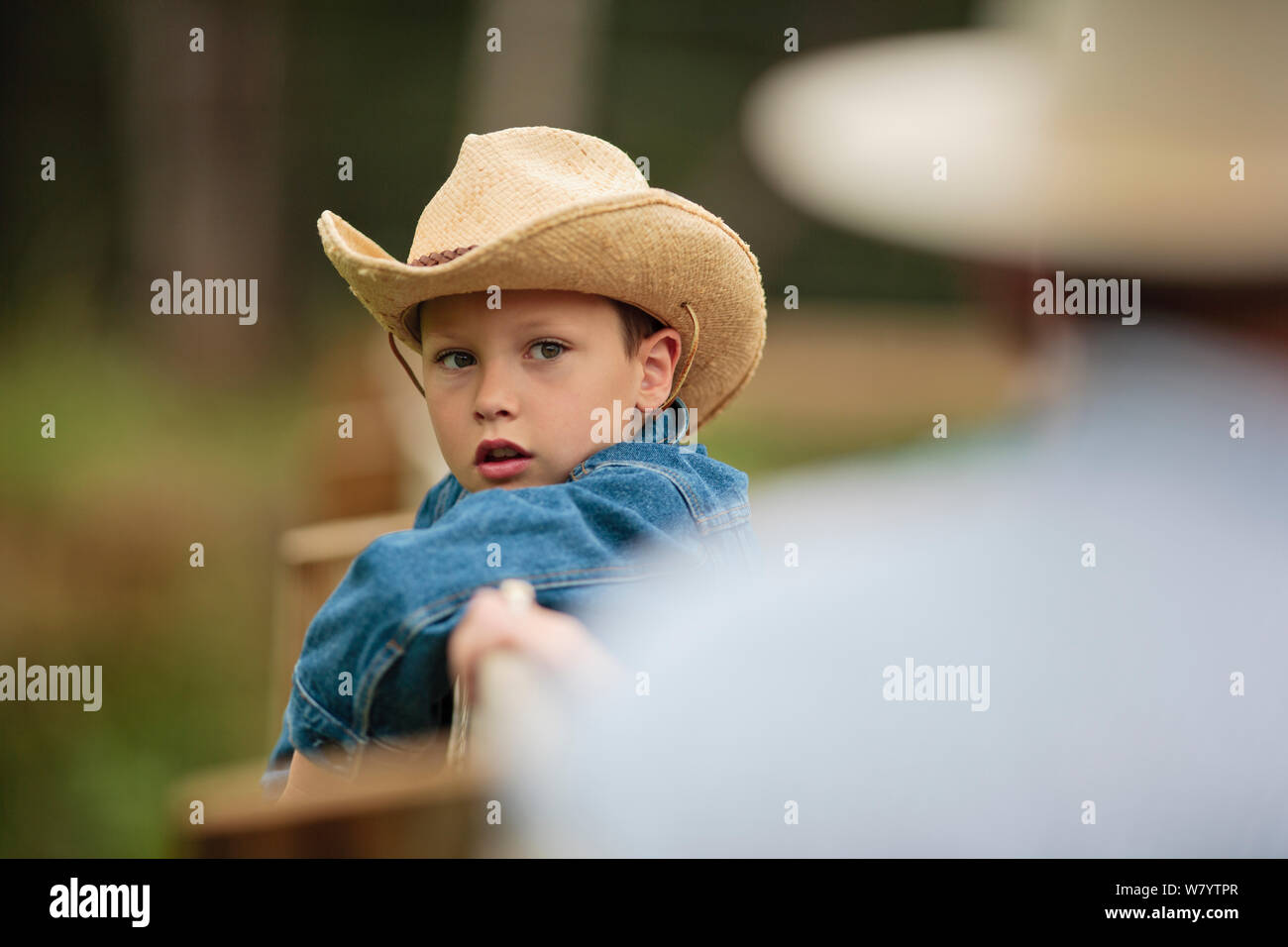 Junge tragen einen Cowboyhut lehnt sich an den Zaun auf einer Ranch und hört zu, wie sein Vater ihm über die Pferde informieren. Stockfoto
