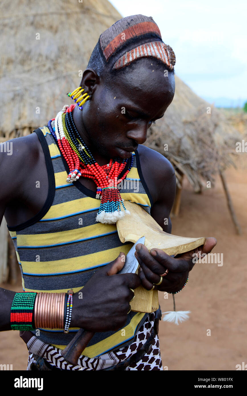 Hamer Mann in traditioneller Kleidung und Schmuck aus Holz schnitzen. Gebiet der hamer Stamm. Untere Omo Tal. Äthiopien, November 2014 Stockfoto