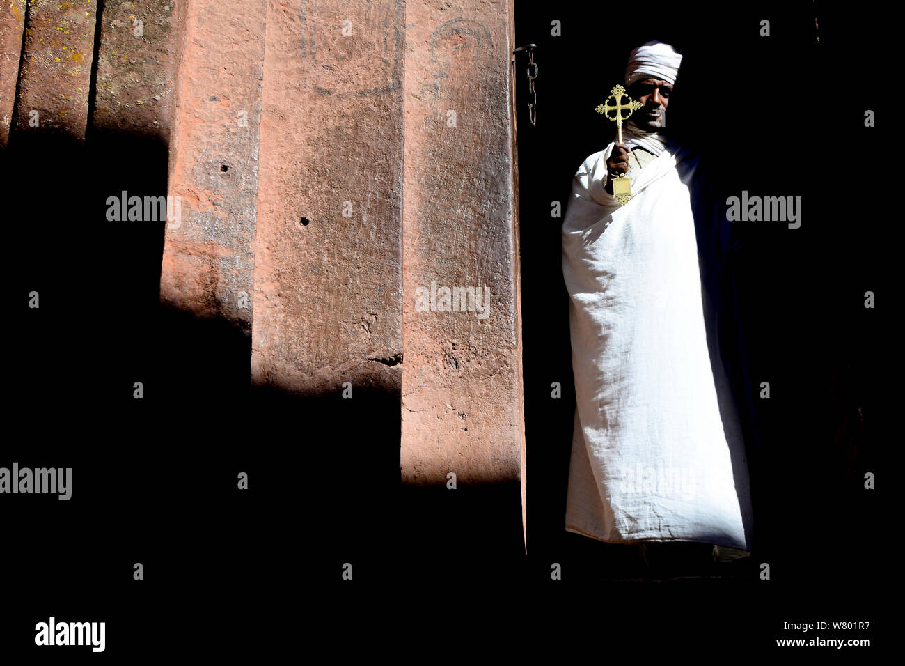 Priester in der traditionellen weißen Gewändern und Turban, mit einem goldenen Kreuz. Wette Giyorgis Kirche, Lalibela. UNESCO-Weltkulturerbe. Äthiopien, Dezember 2014. Stockfoto