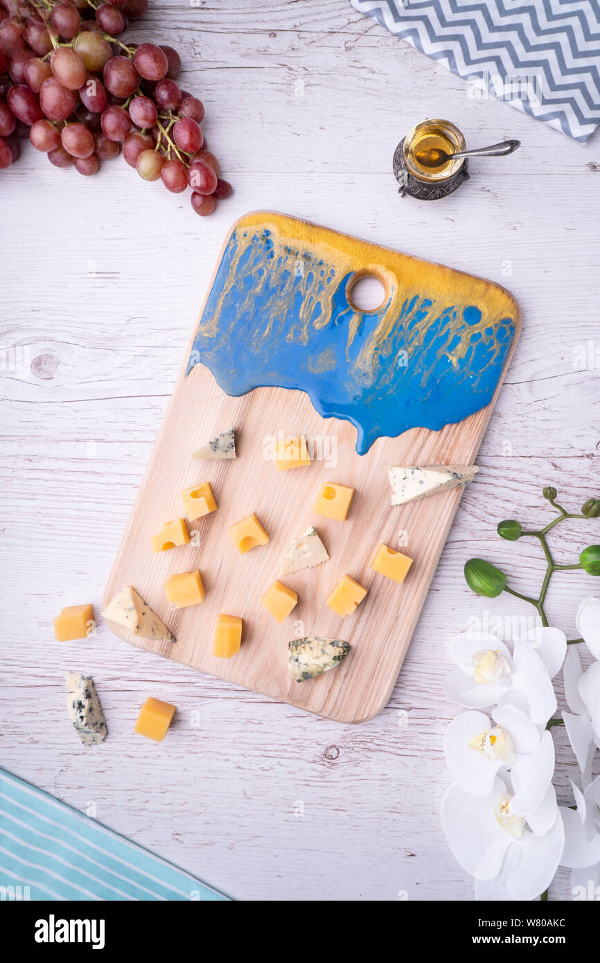 Zusammensetzung Schneidbrett mit einer abstrakten Muster, Käse, Honig, Trauben, Orchidee Blumen, auf hellem Holz der Tischplatte. Stockfoto