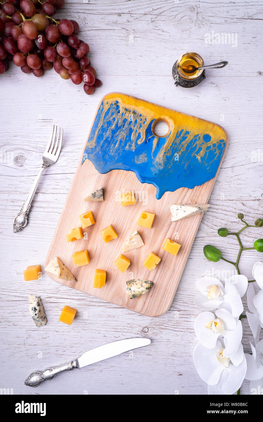 Zusammensetzung Schneidbrett mit einer abstrakten Muster, Käse, Honig, Trauben, Orchidee Blumen, auf hellem Holz der Tischplatte. Stockfoto