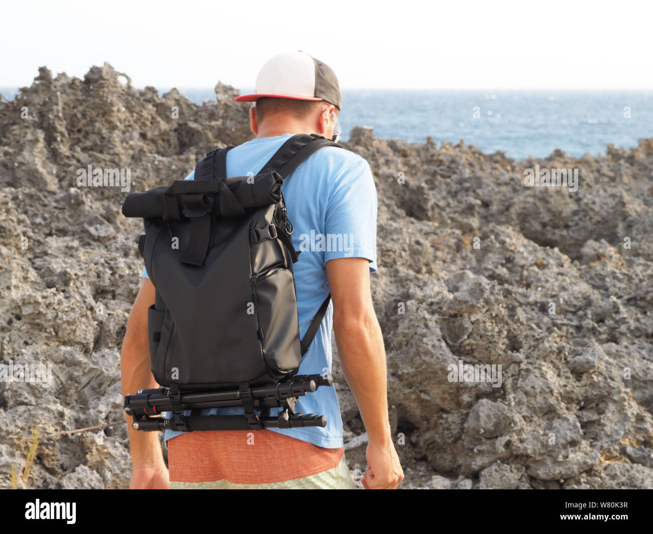 Ein Mann mit einem Rucksack fotografische Geräte auf einem Stein Strand. Urlaub in der Karibik. zurück. Atlantik. Stockfoto