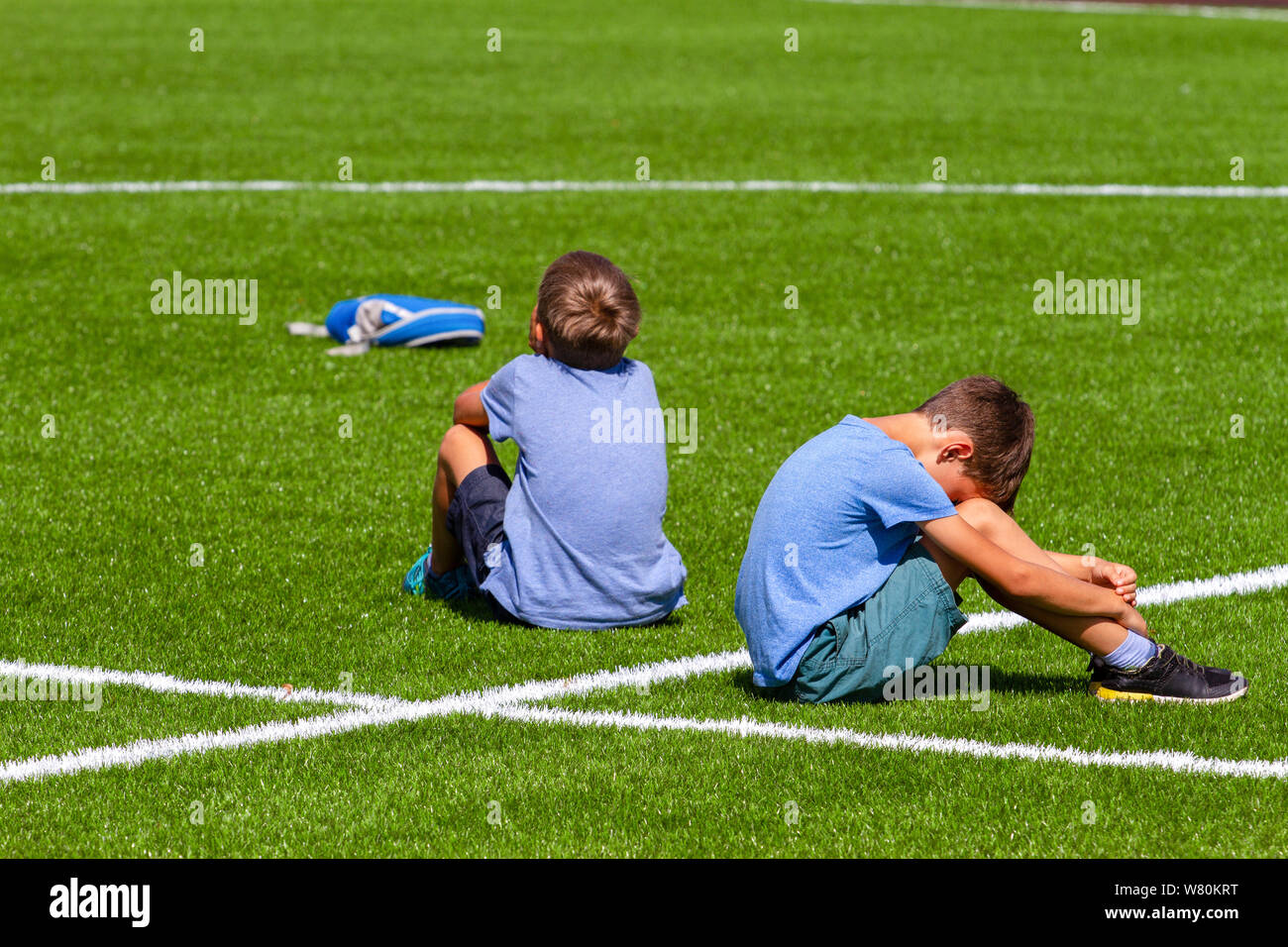 Zwei traurige enttäuscht Jungs Rücken an Rücken sitzen auf dem Rasen im Stadion Stockfoto