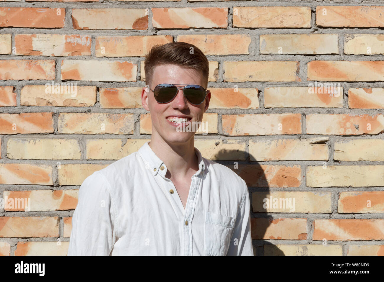 Lächelnden jungen Mann Portrait mit Retro glänzend drop Sonnenbrille gegen Mauer Stockfoto