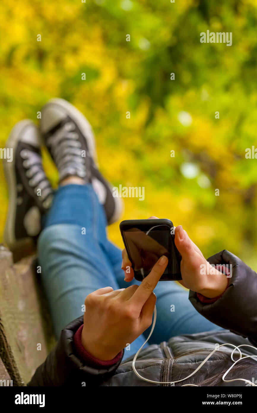 Junges Mädchen mit Smartphone liegen auf der Bank im Herbst Park. Fokus auf Smart Phone. Stockfoto