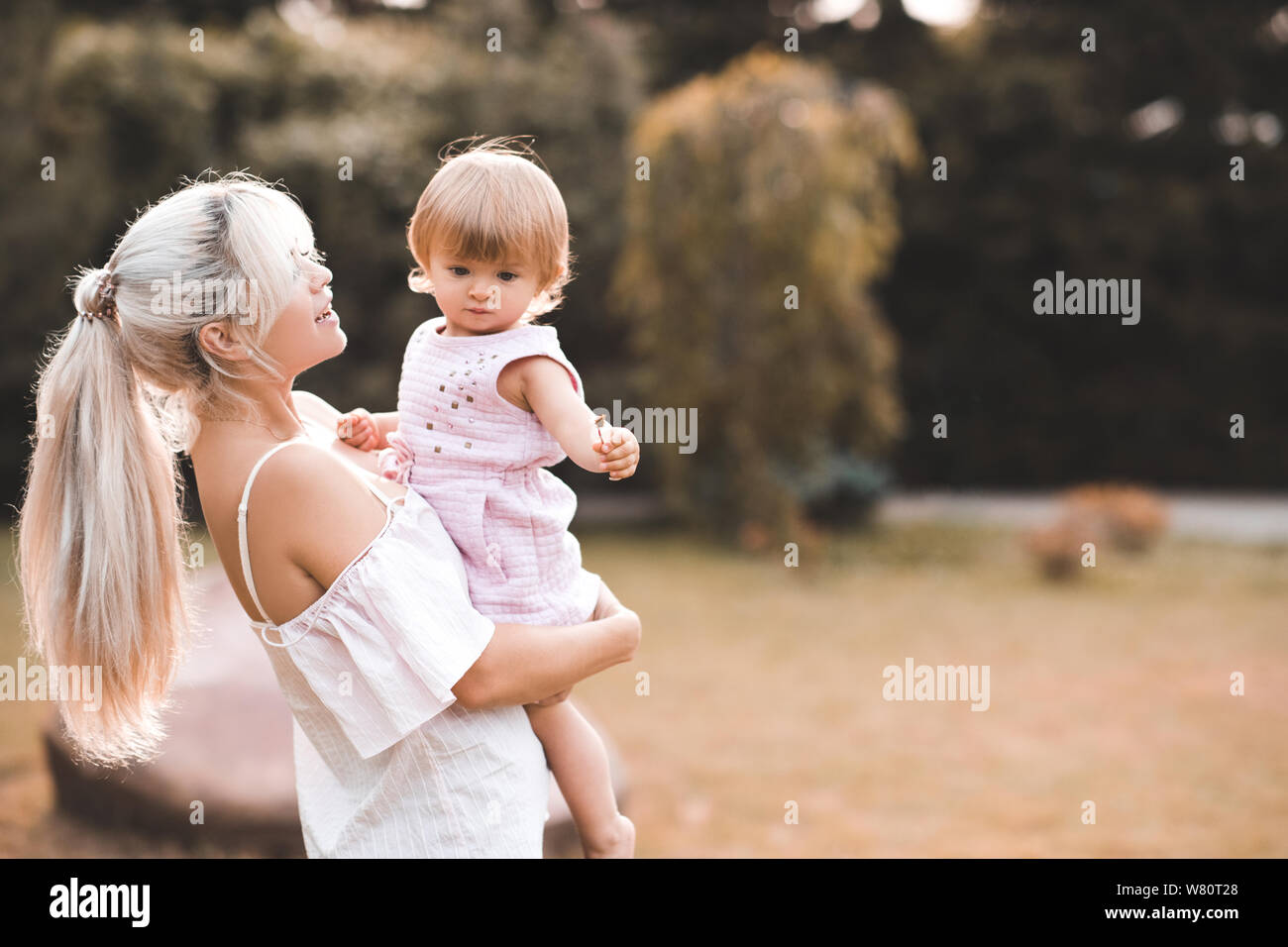 Mutter Holding Baby Mädchen 1-2 Jahre alten stehend in der Wiese im Freien Nahaufnahme. Die Mutterschaft. Mutterschaft. Stockfoto