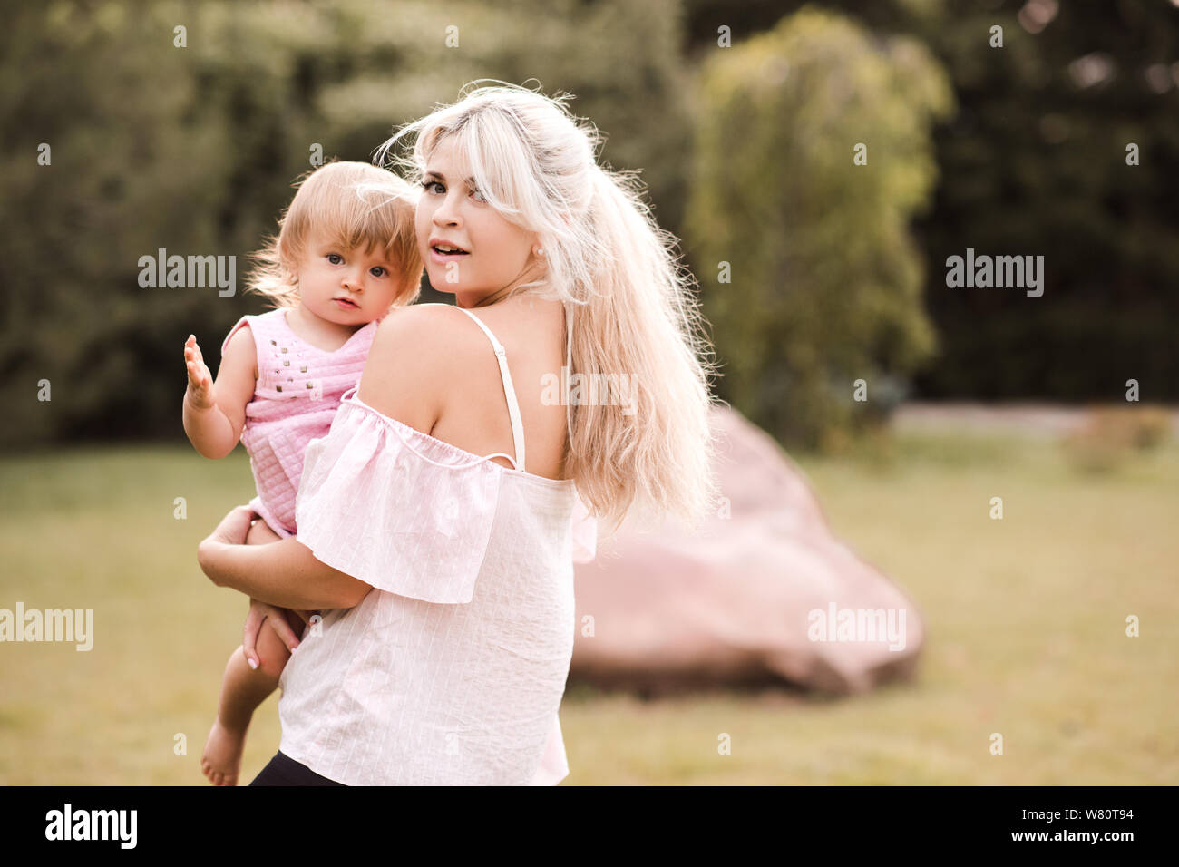 Schöne Mutter durchlöcherte baby girl 1 Jahr alt im Park im Freien posieren. Mit Blick auf die Kamera. Die Mutterschaft. Stockfoto