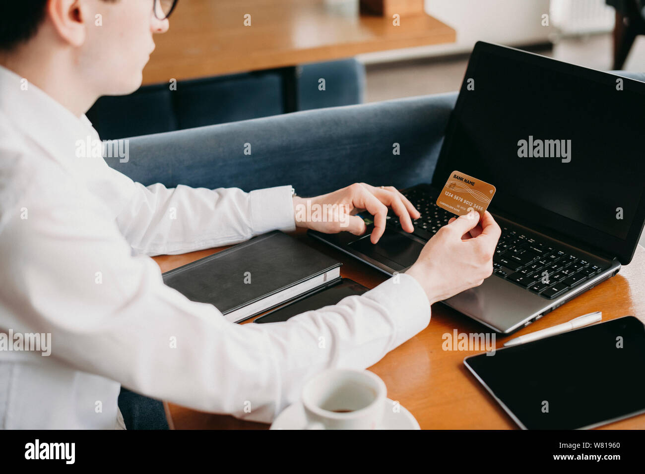 Seitenansicht eines jungen kaukasischen Hand tun Online Transaktion mit einem Gold Kreditkarte und einem Laptop, während in einem Café sitzen. Stockfoto