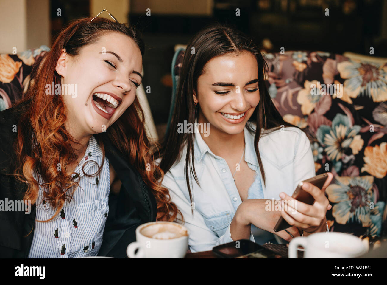 Reizende junge Frau plus größe Spaß Lachen mit geschlossenen Augen, während ihre Freundin etwas auf Ihrem Smartphone zeigte, während Kaffee trinken in einem c Stockfoto