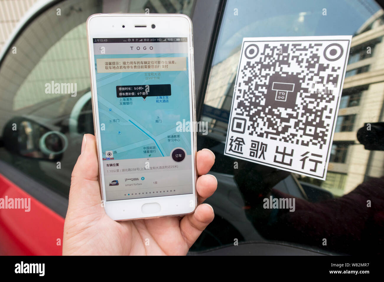 Eine chinesische Benutzer bereitet die TOGO App auf seinem Smartphone den QR-Code zu scannen ist ein Mercedes-Benz Smart Fortwo von Auto-sharing Service TOGO auf Stockfoto