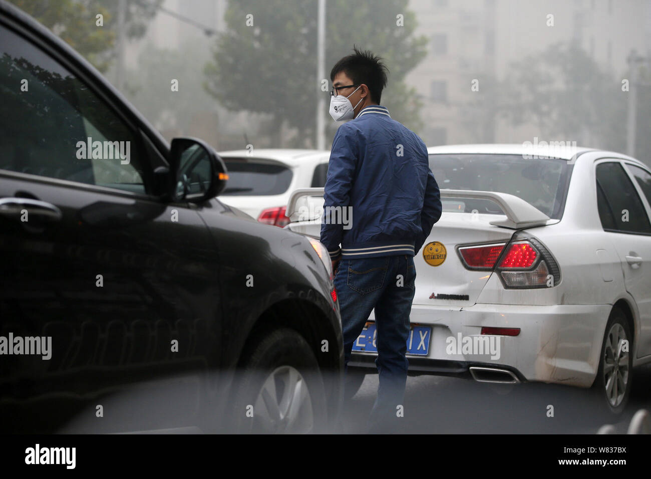 ---- Ein fussgänger Tragen einer Schutzmaske gegen die Verunreinigung der Luft Spaziergänge durch Autos auf der Straße in schweren Smog in Peking, China, 14. Oktober 2016. Beij Stockfoto