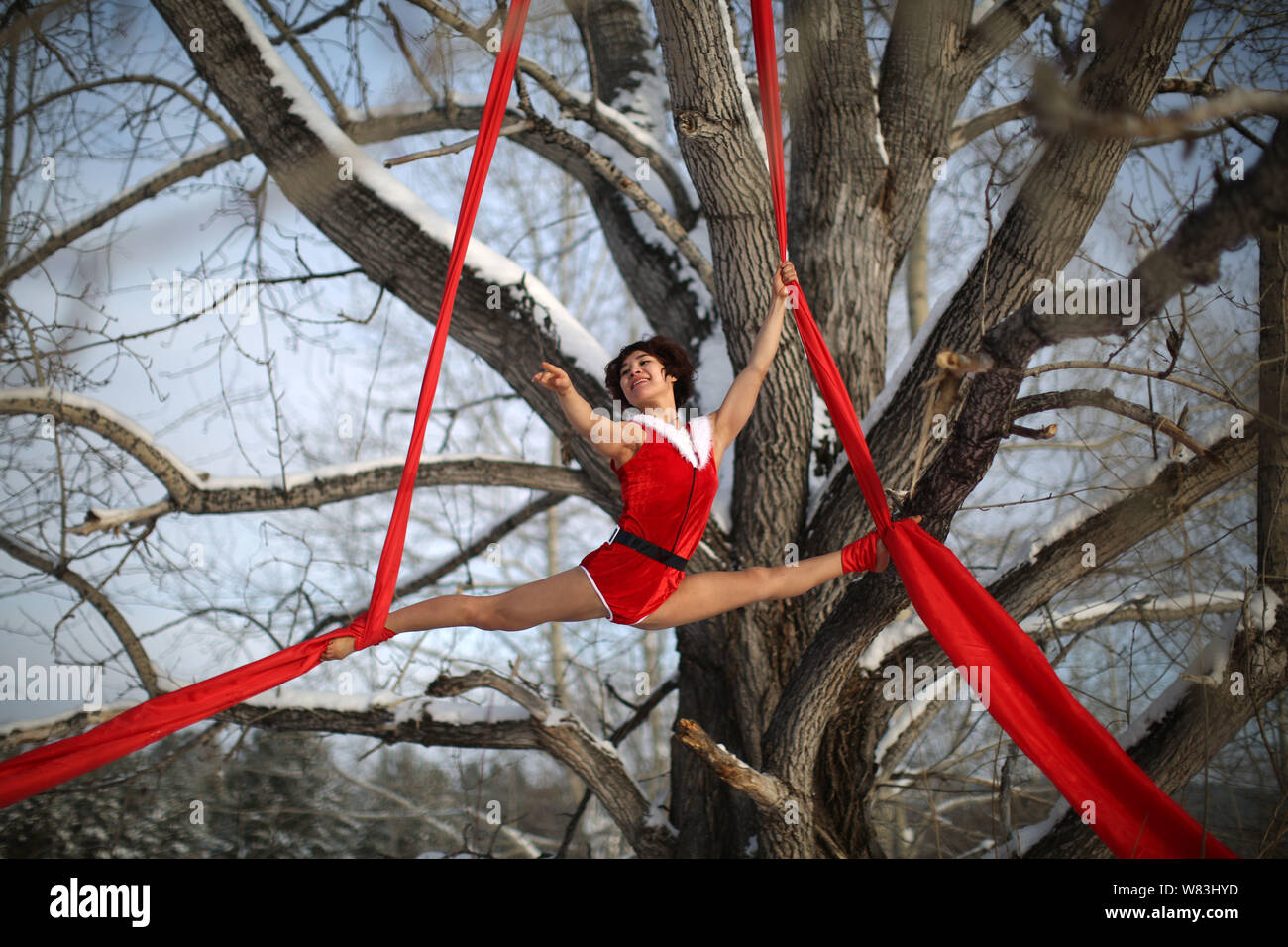 Eine weibliche Chinesische Pole Dancer in Weihnachten Kostüm führt mit einem roten Band hängend an einem Baum Weihnachten im Schnee in Mohe coun zu feiern. Stockfoto